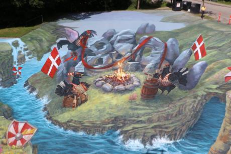 3D-gadekunst med dansk tema, bål omgivet af sten, flag og vand.